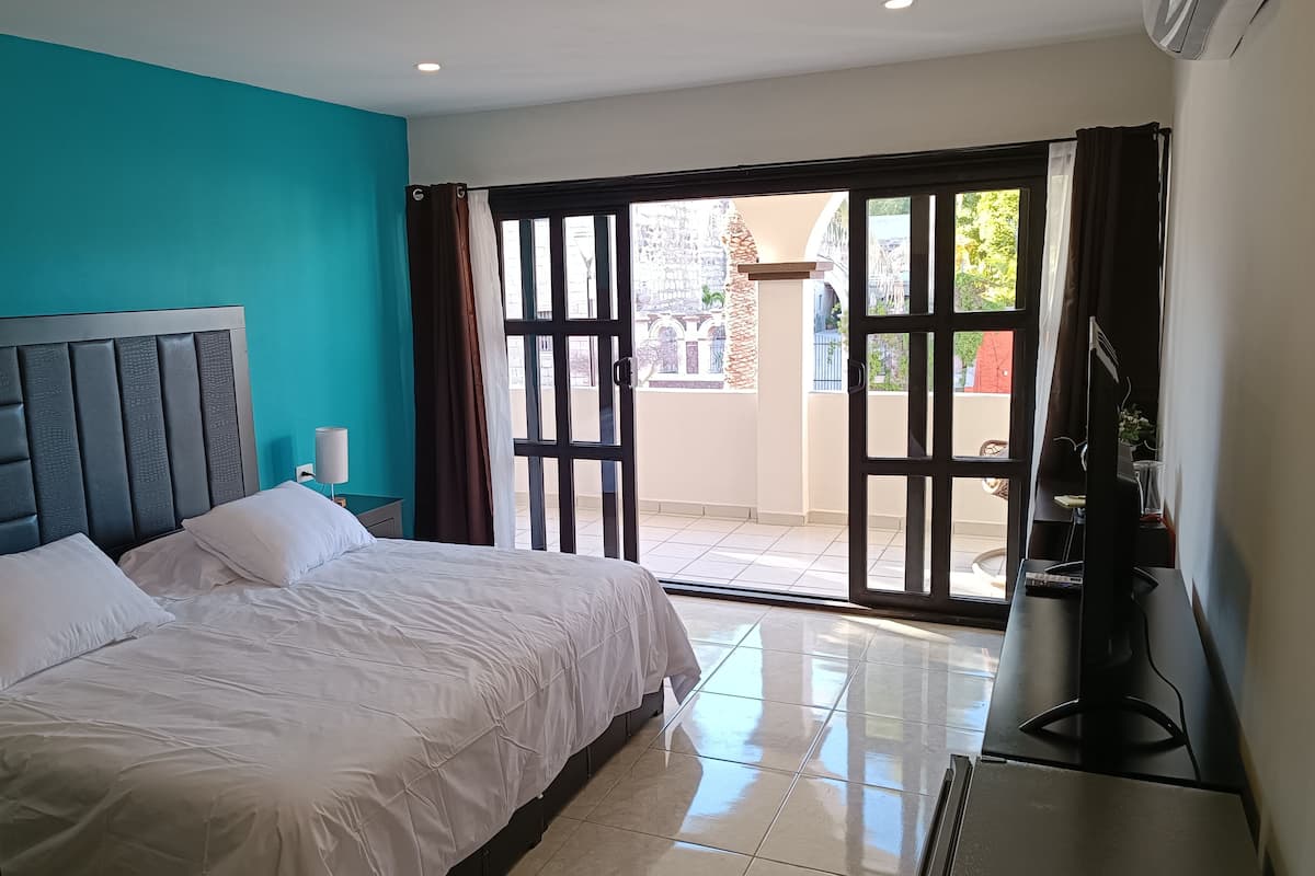Habitación de hotel con cama, televisor y puerta corrediza de vidrio que da a un balcón.