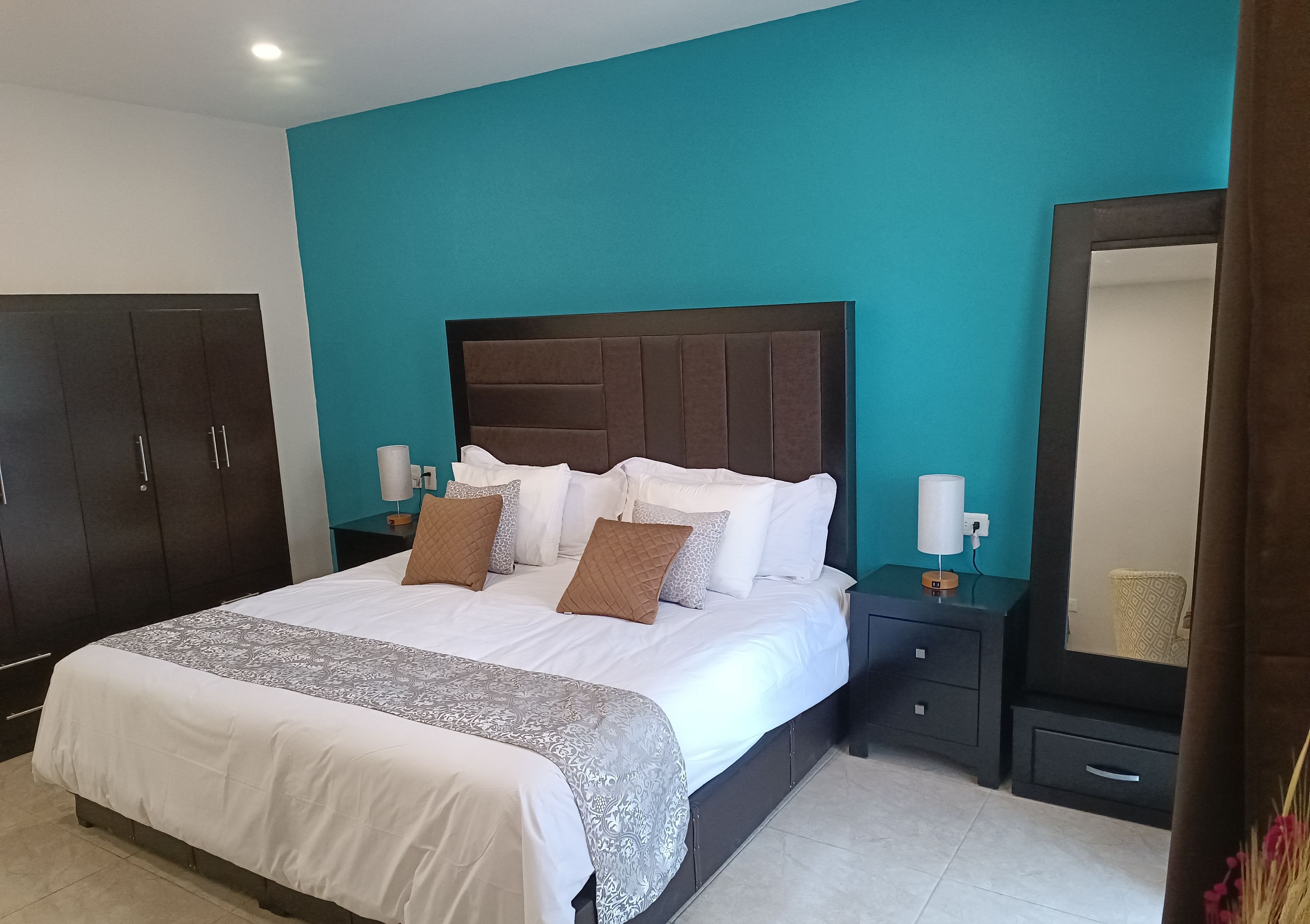 Una habitación de hotel con una cama grande, un armario, una mesita de noche con lámpara y un espejo.
