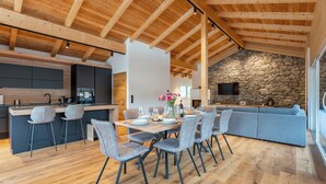 Une cuisine spacieuse avec un mur en pierre et un coin repas doté de chaises modernes et d’une table en bois.