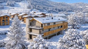 Une station de montagne enneigée, avec des bâtiments en bois, un télésiège et un ciel dégagé.