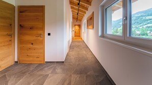 Un couloir avec des portes en bois, un sol carrelé et une grande fenêtre donnant sur un paysage vallonné.