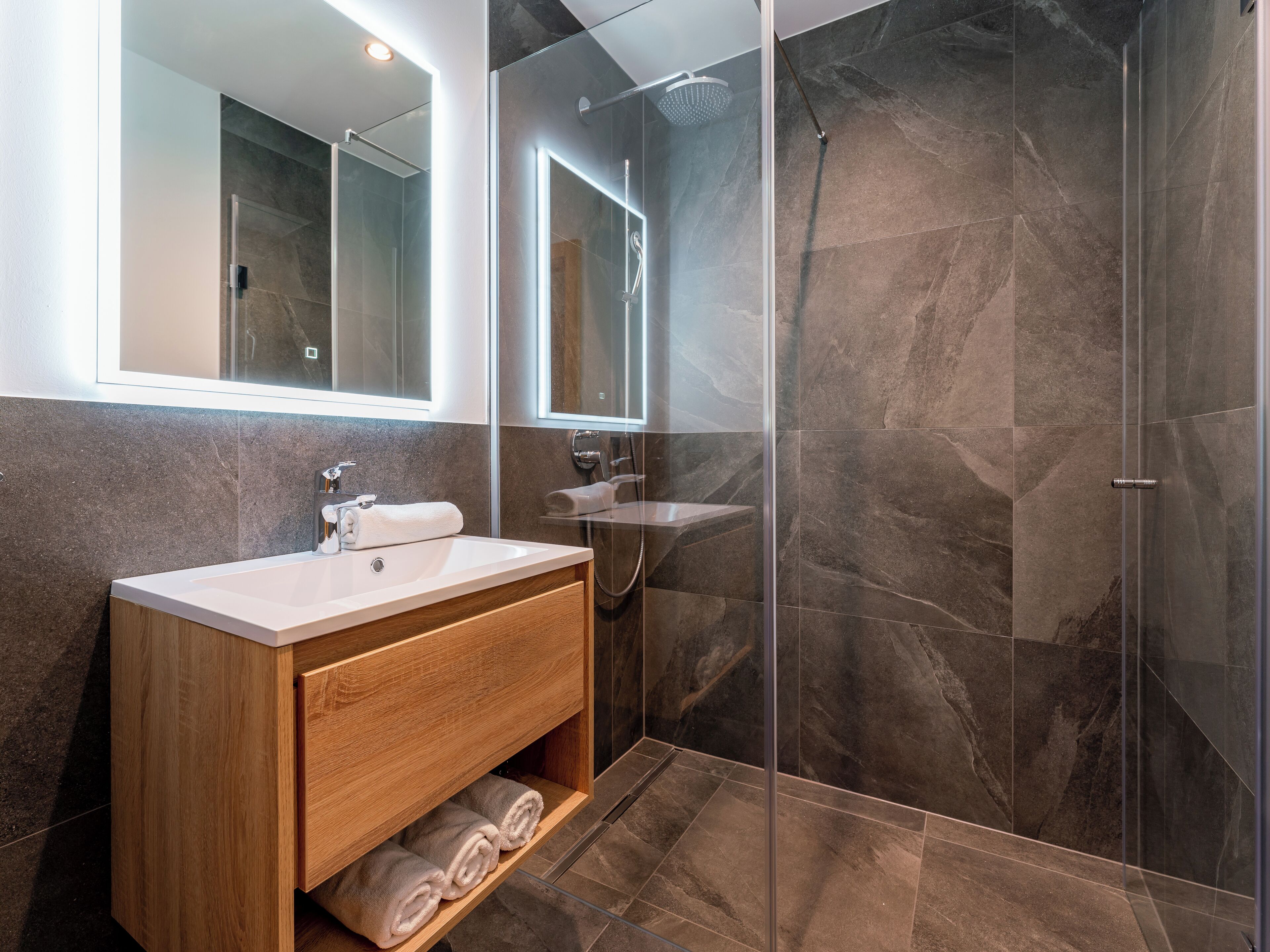 Un bagno moderno con doccia vetrata, mobile bagno in legno con lavello e specchio sopra il mobile.