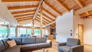 Un vaste espace de vie doté d’un plafond en bois, d’un canapé, d’une table basse et offrant une vue sur la cuisine et l’espace extérieur aménagé pour se détendre.