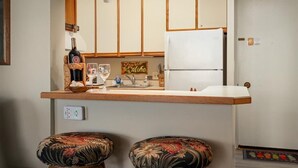 A compact kitchen with a wooden countertop, a white refrigerator, and two upholstered stools.