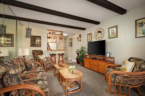 Uma sala de estar com sofá, cadeiras, mesa de centro, rack para TV e estante.