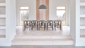 Un comedor con una mesa larga y sillas, techo abovedado con vigas de madera y un gran ventanal que proporciona luz natural.