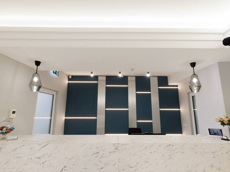 Een modern receptiebalie met een marmeren blad, verlichting erboven en een digitale klok die de tijd toont.