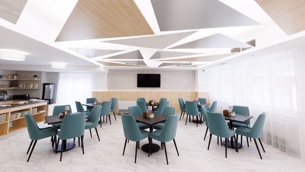Un comedor moderno con diseño geométrico en el techo, varias mesas y sillas, y una cocina al fondo.