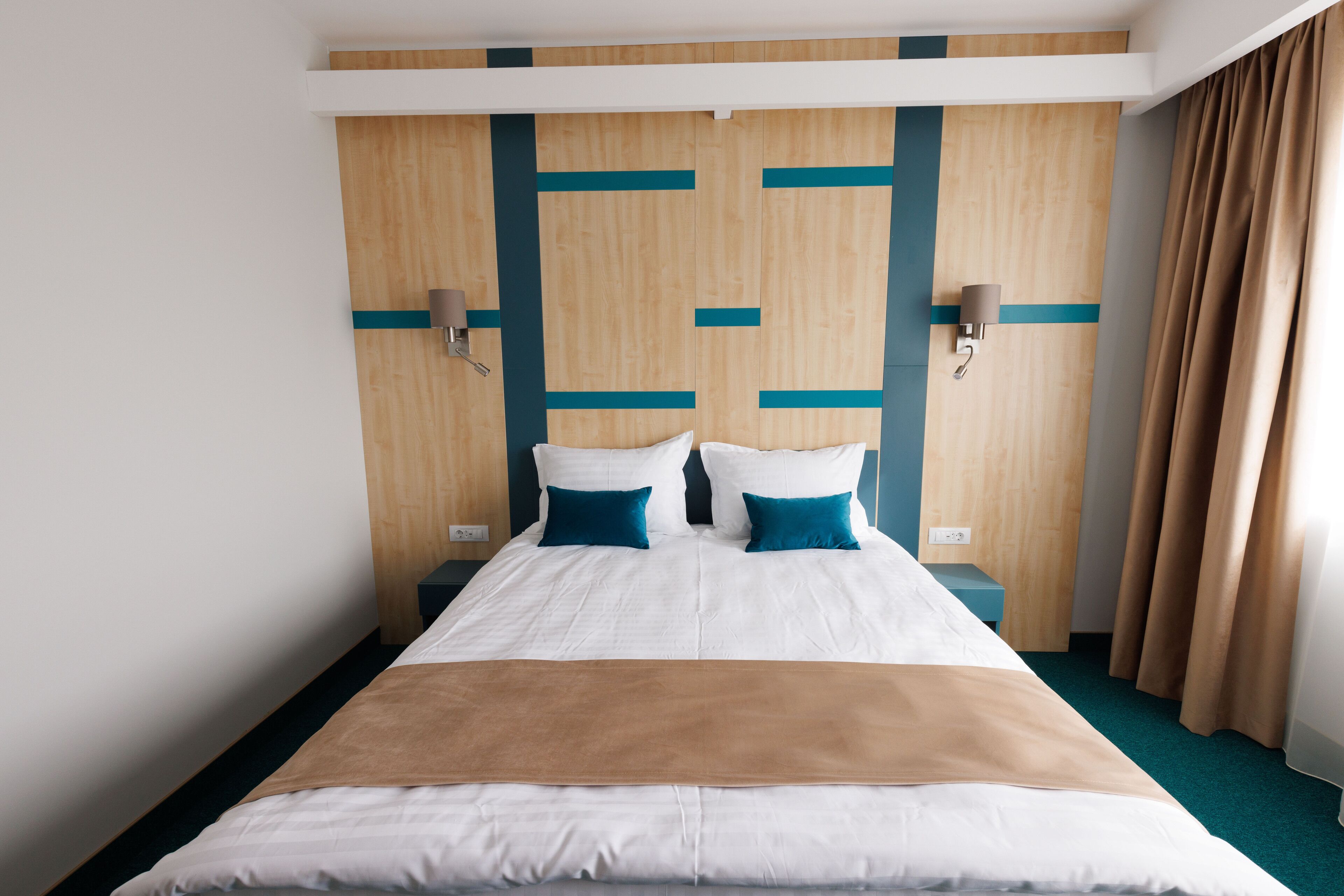 A hotel room with a large bed, wooden headboard, two wall-mounted lamps, and a window with curtains.