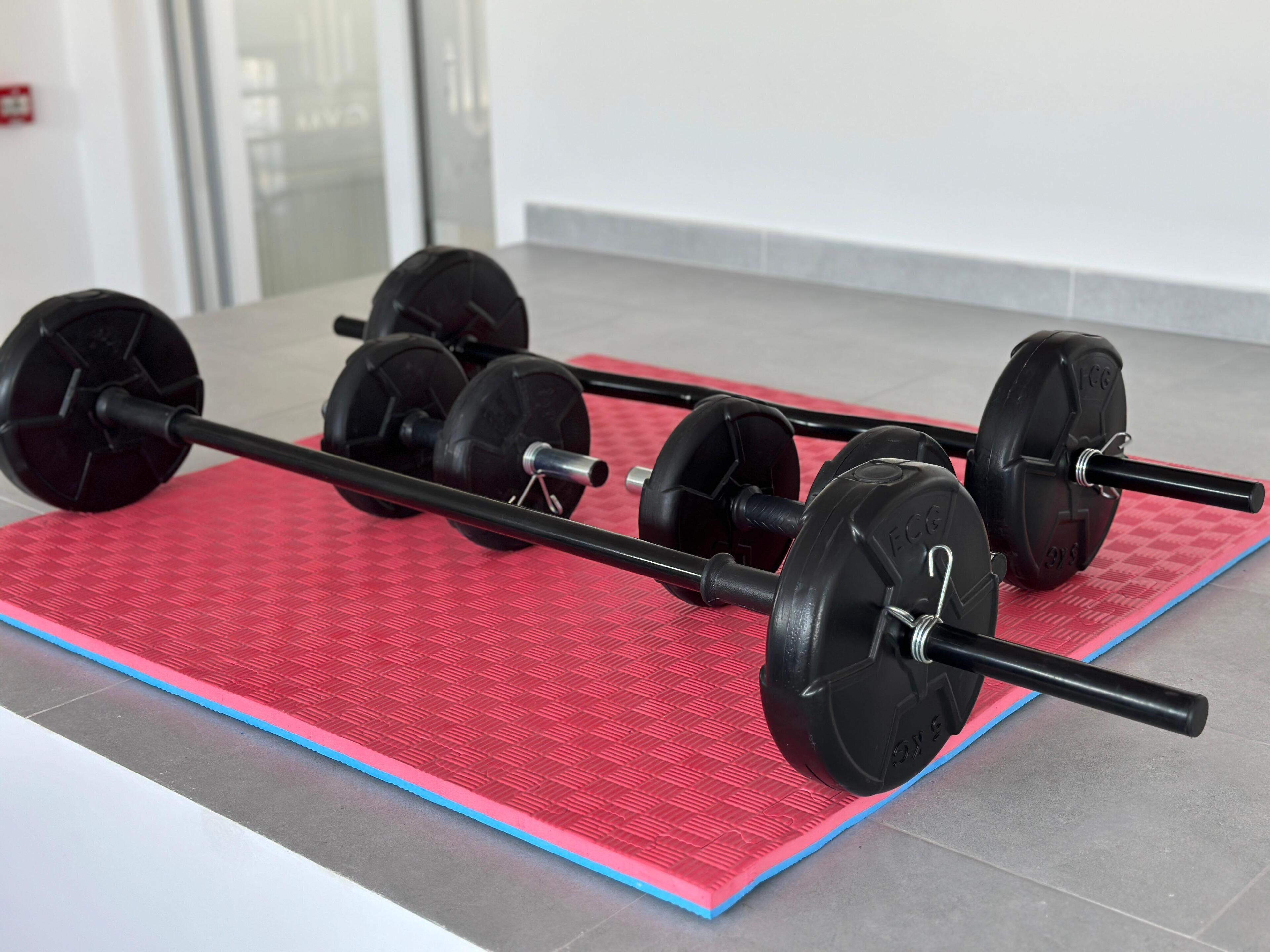 A barbell with weights on a red mat in a room with a tiled floor and a white wall.