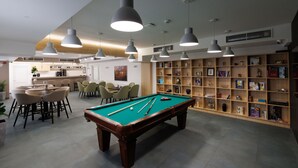 Una mesa de billar en una habitación con comedor, estanterías e iluminación colgante.