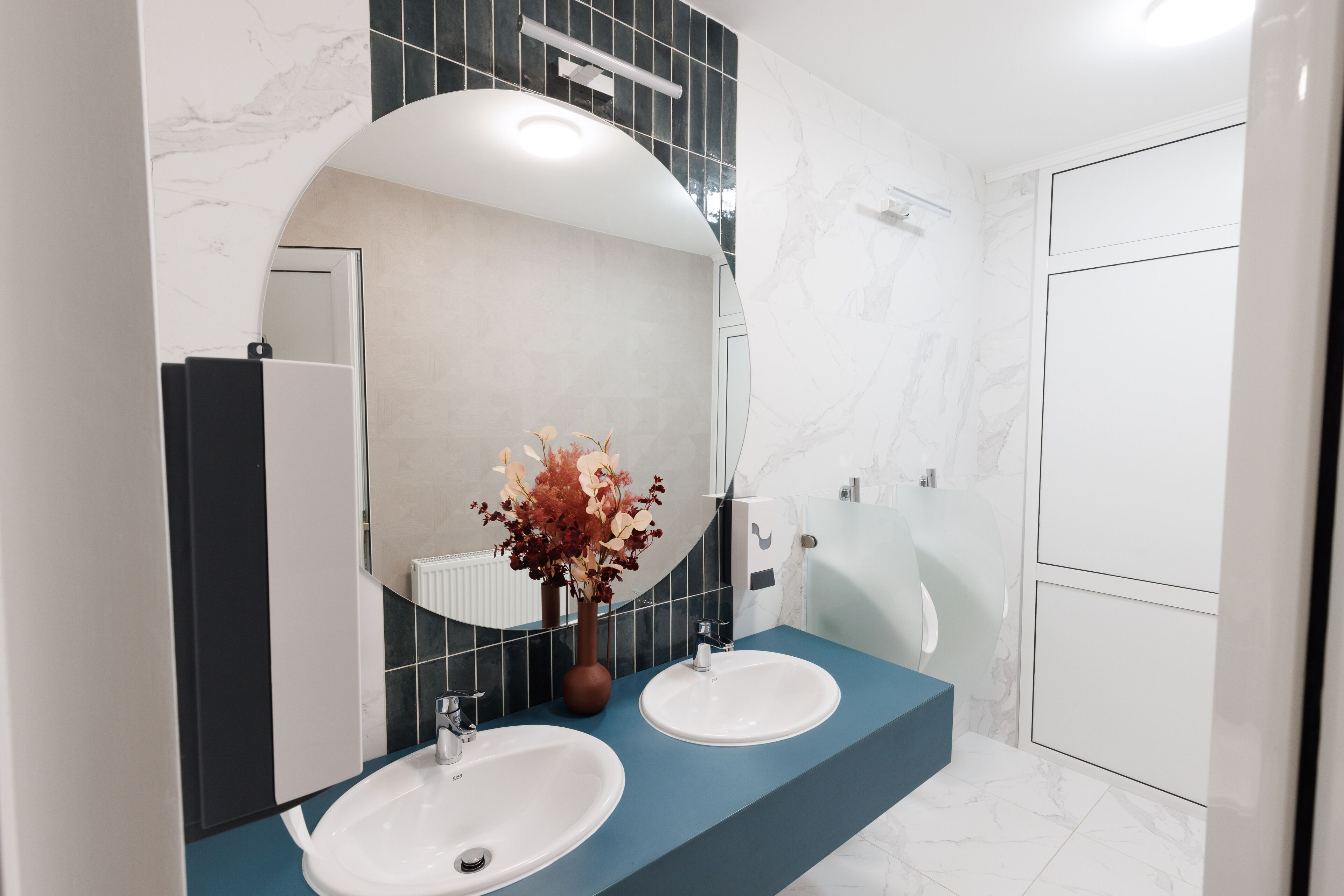 Un baño moderno con dos lavamanos, un espejo grande y un florero con flores.