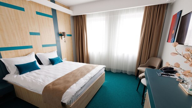 A hotel room with a large bed, a desk, a chair, and a window with curtains.