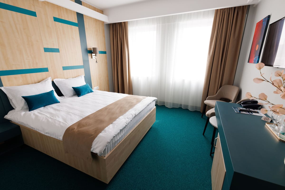Una habitación de hotel con una cama grande, un escritorio, una silla y una ventana con cortinas.