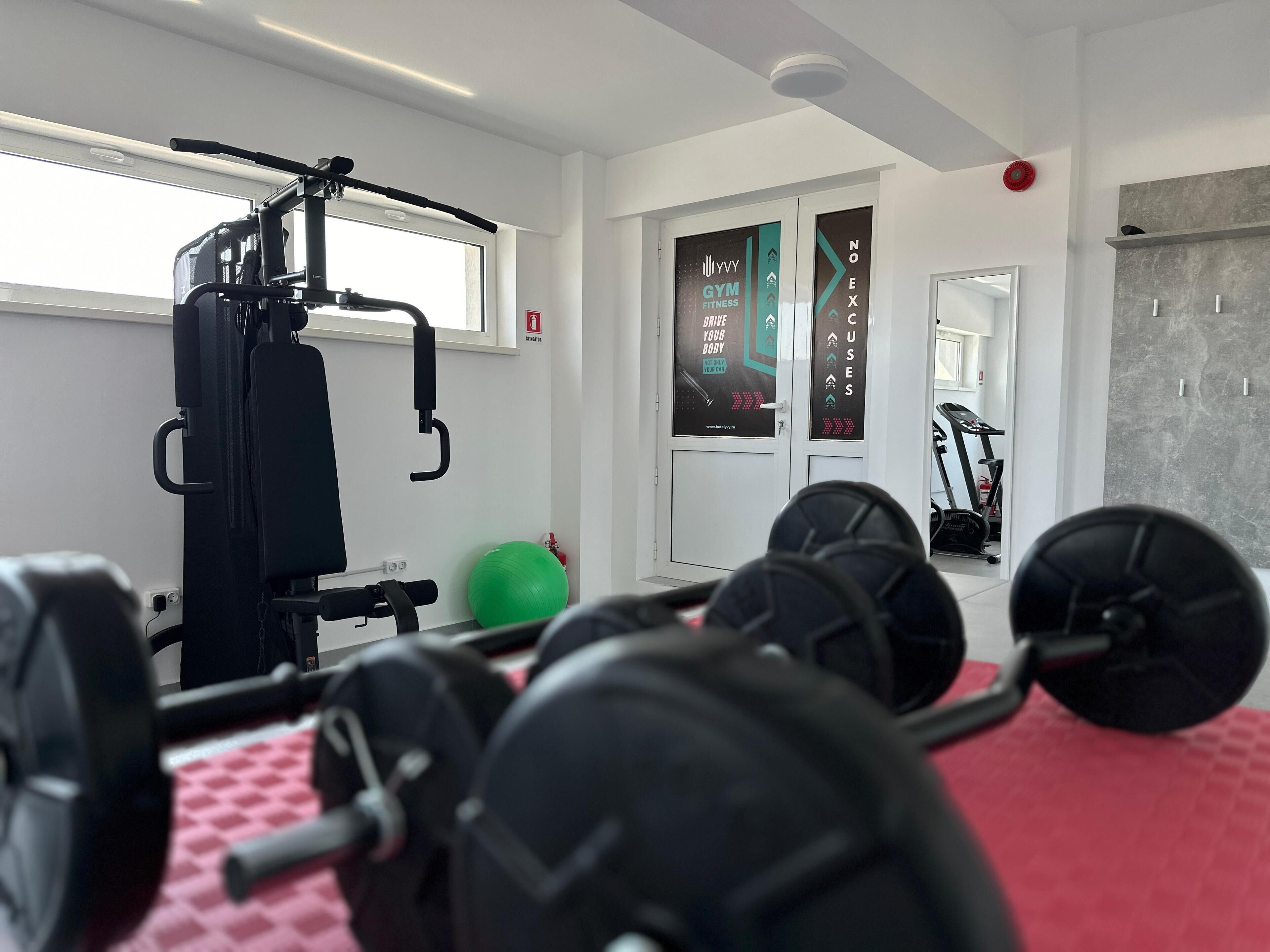 Un gimnasio con equipo de ejercicio, una pelota de ejercicio verde y una colchoneta roja.