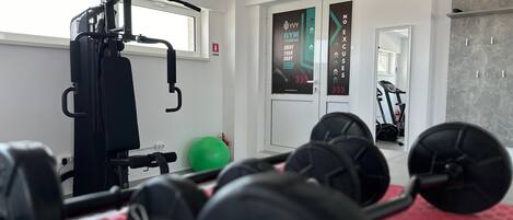 Un gimnasio con equipo de ejercicio, una pelota de ejercicio verde y una colchoneta roja.