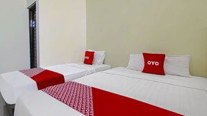 Una habitación de hotel con dos camas individuales, cada una con una colcha blanca y un cojín rojo con la marca 'OYO'.