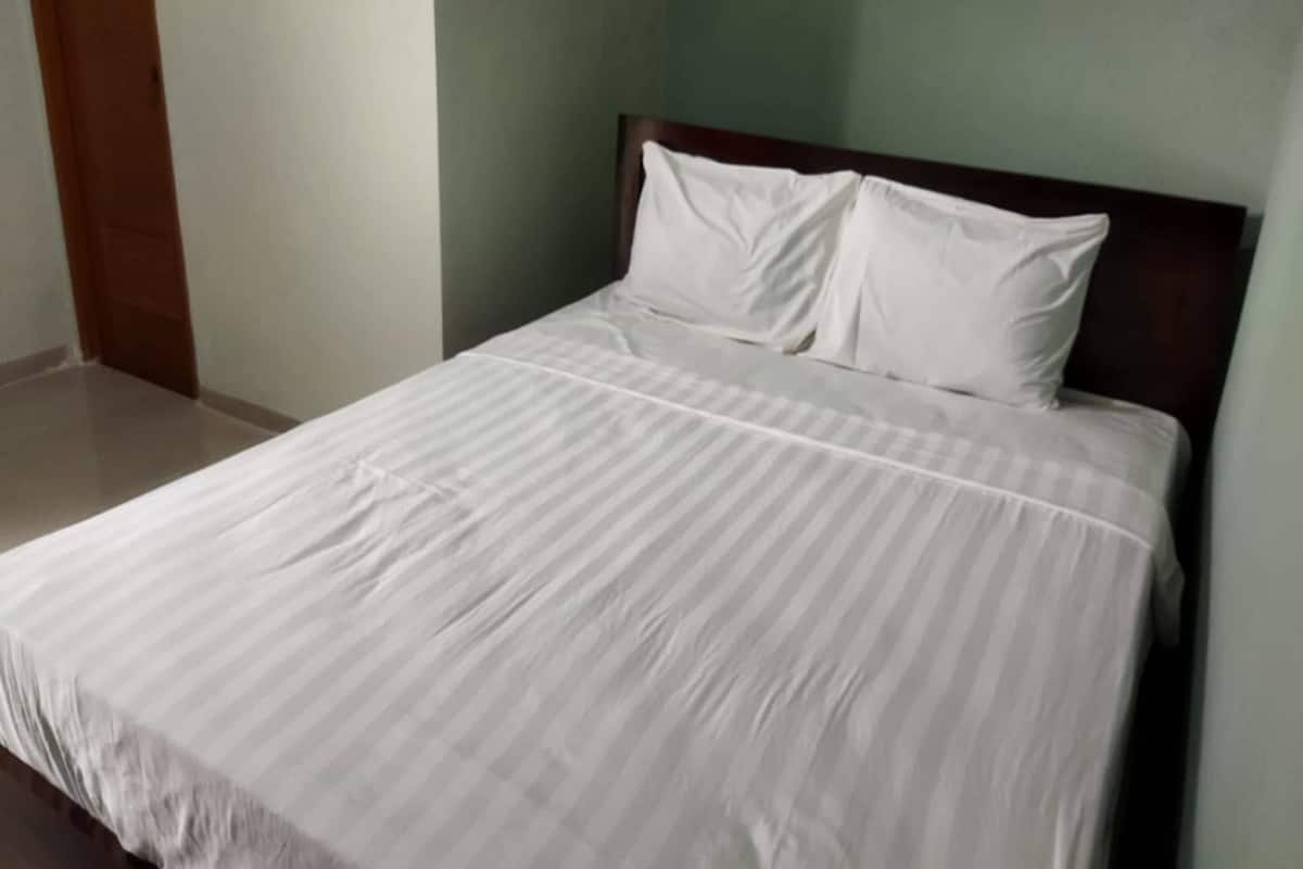 Una cama con cabecera de madera, una colcha blanca y dos almohadas blancas.