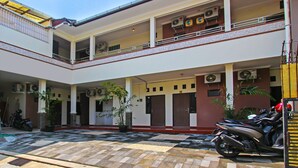 Un edificio de varios niveles con un patio empedrado, unidades de aire acondicionado y una motocicleta estacionada afuera.