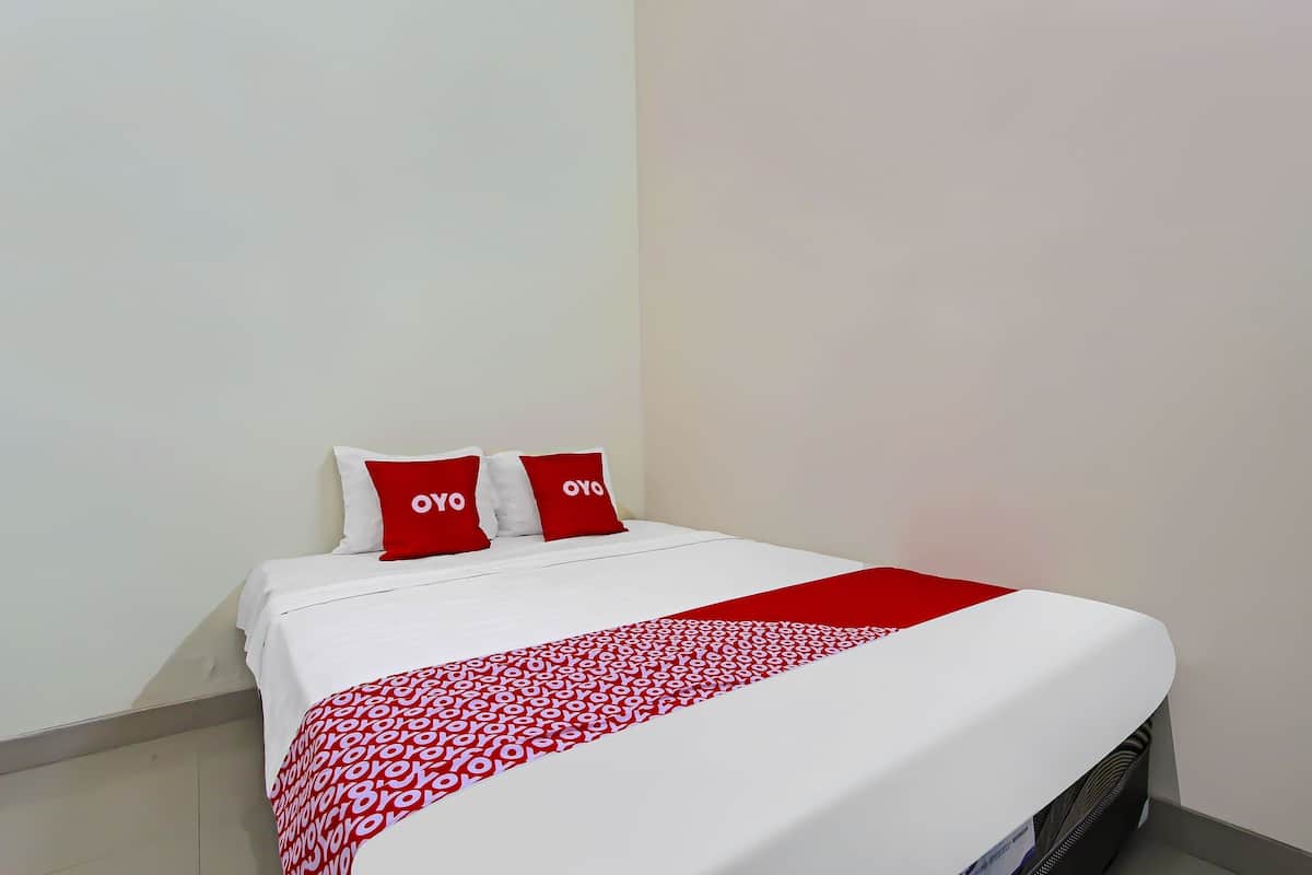 Una cama bien hecha con una colcha blanca y roja, dos almohadas con la palabra 'OYO' y una manta roja.