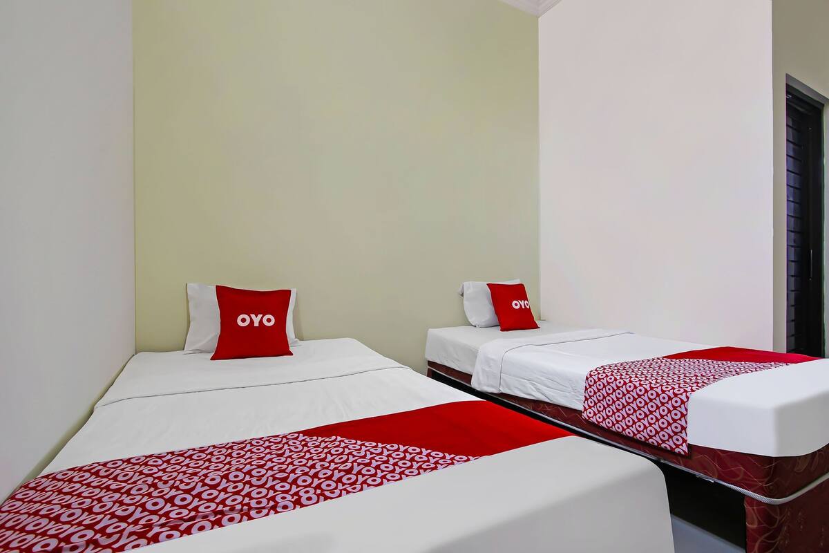 Dos camas individuales con ropa de cama roja y blanca, una manta estampada en rojo y blanco, y una pared de color verde claro.