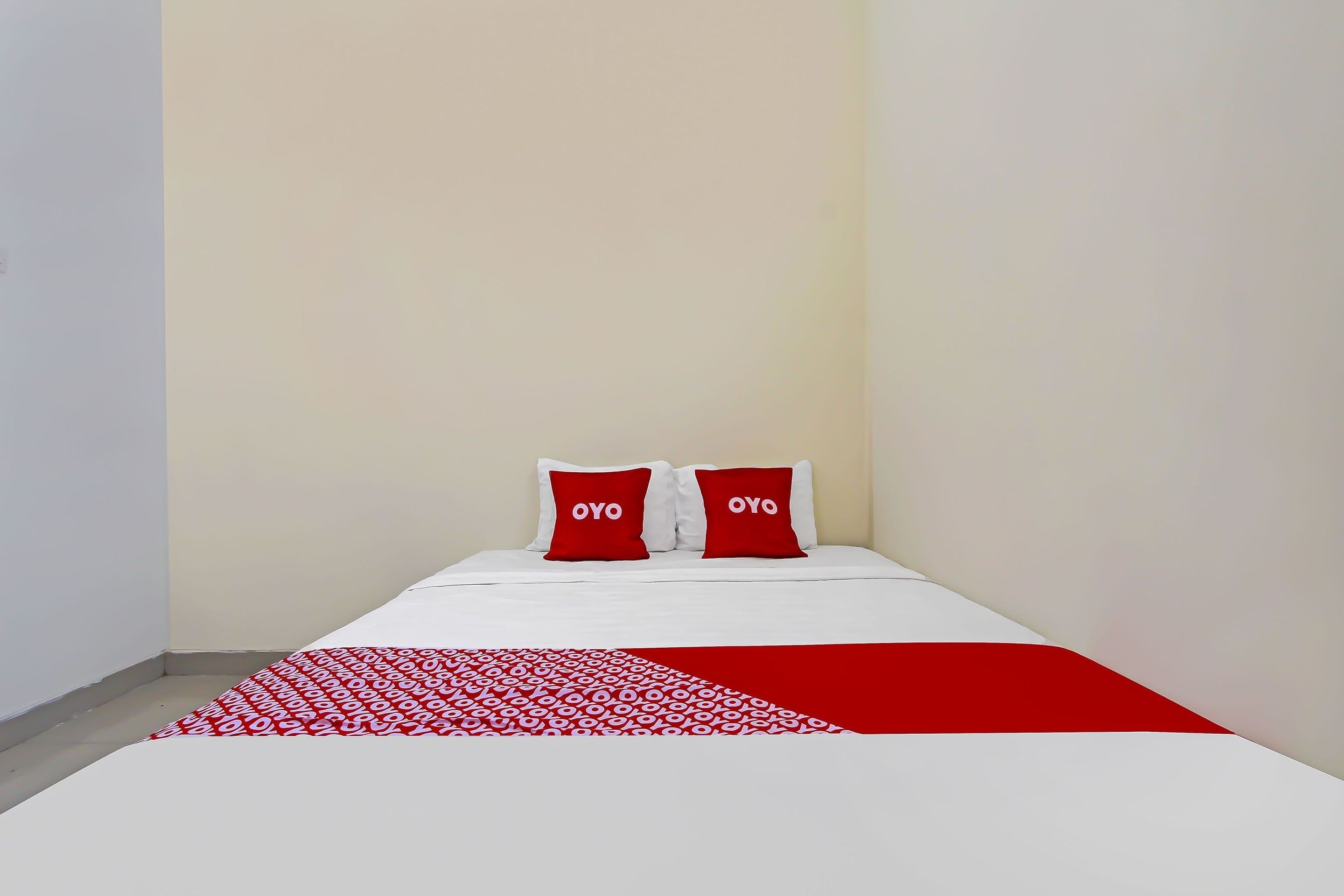 A hotel room with a bed, two pillows with the word "OYO" on them, and a red and white patterned throw blanket.