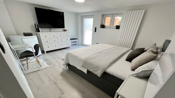 A modern bedroom with a bed, dresser, and TV. - 2 room apartment, comfortable, king size bed, TV (Hannover)