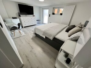 A modern bedroom with a bed, dresser, and TV. - Comfortable 2-room apartment with a king-size bed and TV (Hannover)