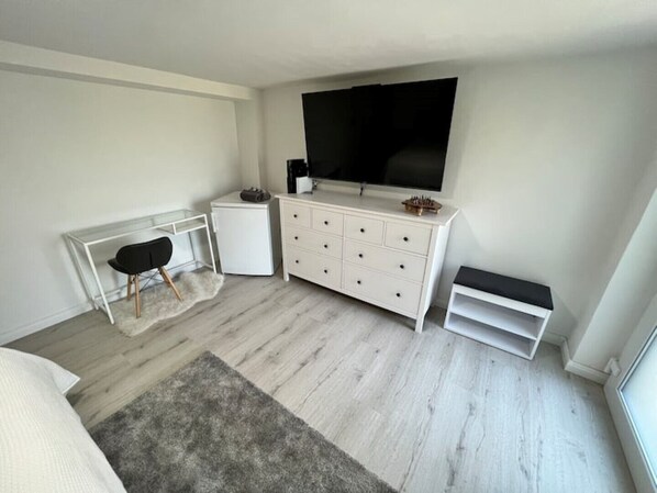 A modern bedroom with a bed, a desk, a dresser, a TV, and a small white cabinet. - Comfortable 2-room apartment with a king-size bed and TV (Hannover)