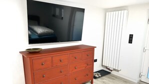 A room with a wooden dresser, a flat-screen TV mounted above it, a white radiator, and a door with a mat. - 2 room apartment, comfortable, king size bed, TV (Hannover)