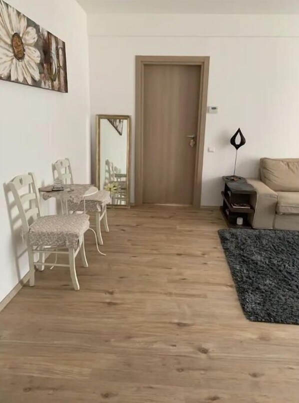 A living room with a wooden floor, a sofa, a coffee table, and a dining area with chairs and a table.