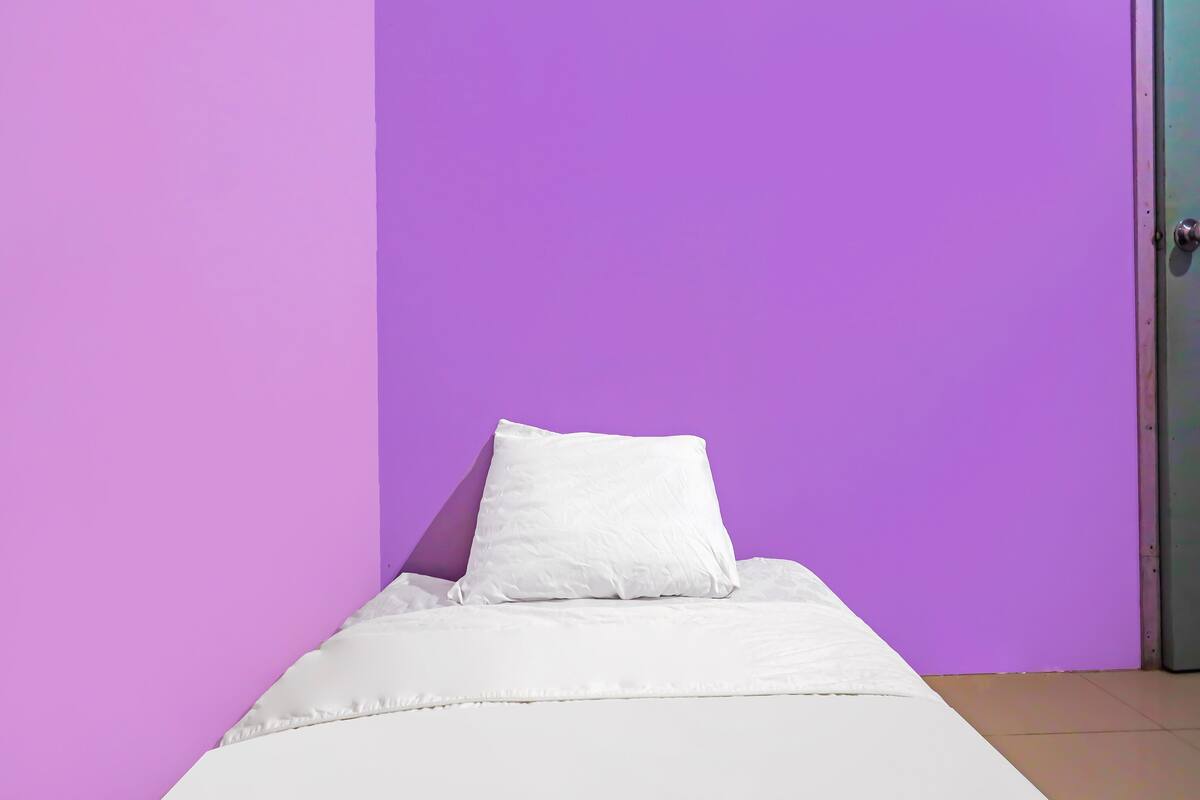A single bed with white bedding in a room with purple walls and a closed door.