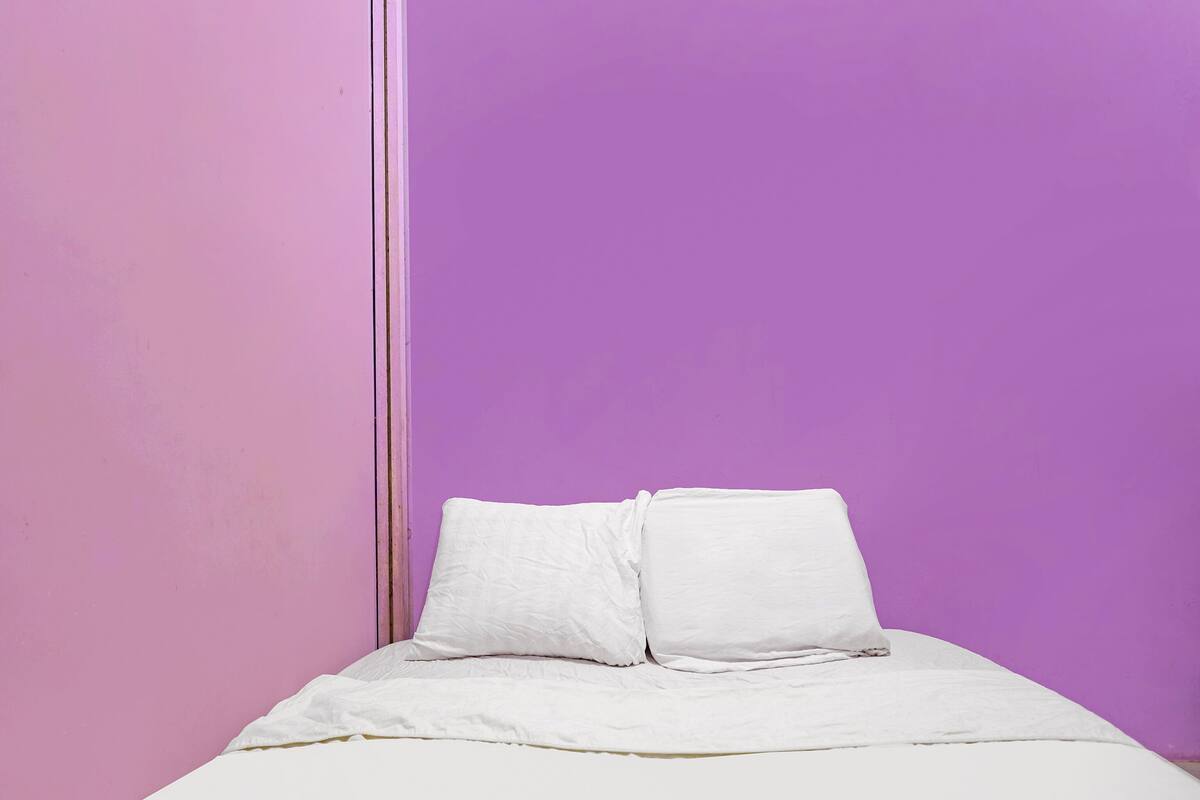 A single bed with white bedding in a room with pink and purple walls.