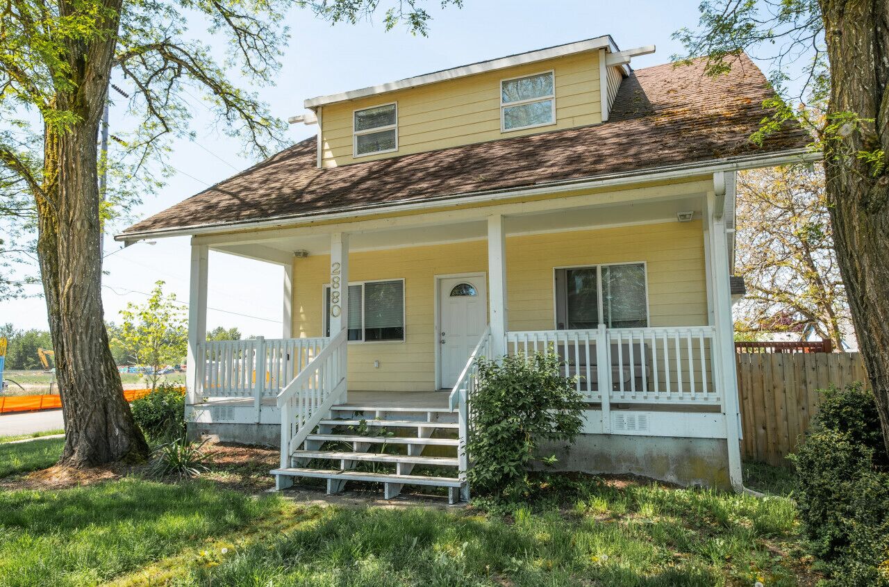 A two-story yellow house with a porch, a front door, and a small front yard.