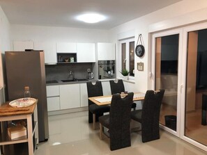 A modern kitchen with white cabinets, a dining table with four chairs, a refrigerator, and a coffee maker.