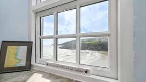 Een kamer met een groot raam dat uitkijkt op een strand, een ingelijste kaart en een plaquette op de vensterbank.