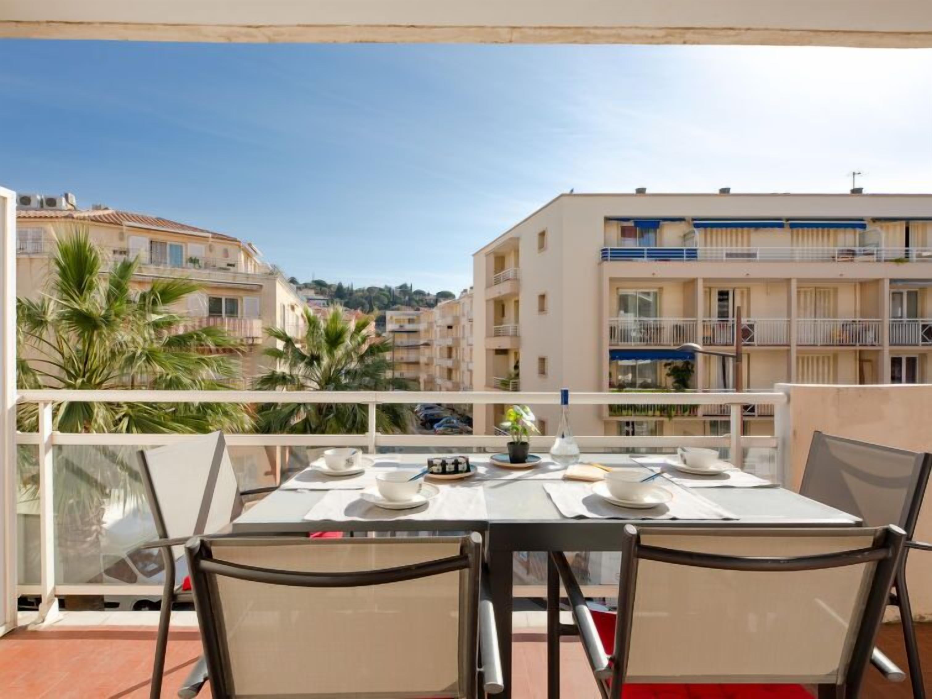 Un balcon avec une table dressée pour deux personnes, donnant sur un quartier résidentiel avec des immeubles et des palmiers.