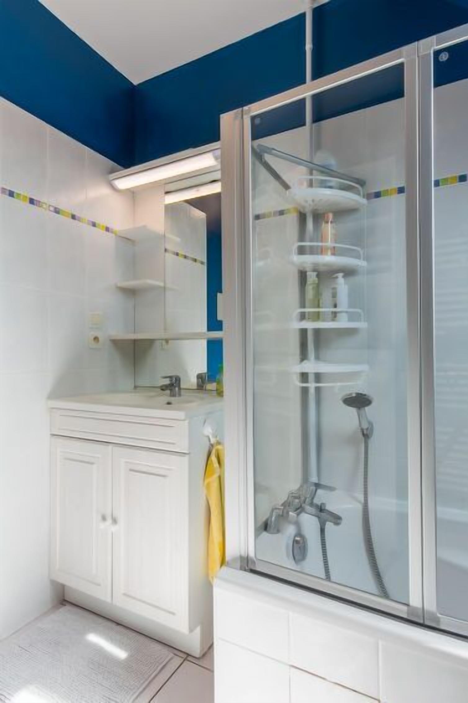 A modern bathroom with a white vanity, a glass-enclosed shower, and a blue accent wall.