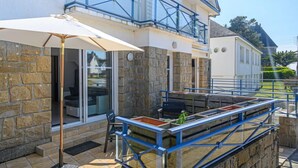 Ein Gebäude mit einer Stein-Fassade, einem Balkon mit blauen Geländern und einem Tisch mit Stühlen unter einem weißen Sonnenschirm.