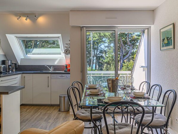 A modern kitchen with a skylight, a dining area with a glass table, and a view of trees through large windows.