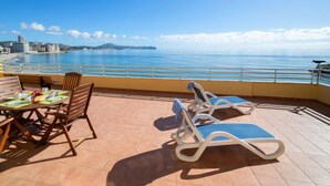 Terraço com mesa posta para refeições, duas espreguiçadeiras e vista para o mar e a paisagem urbana.