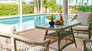 Un espace aménagé au bord de la piscine, avec des meubles en osier, une table en verre et un saladier rempli de fruits.