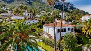 Une villa en bord de mer, dotée d’une piscine, entourée de palmiers et surplombant un paysage montagneux.