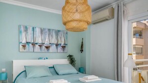 Une chambre à coucher avec un lit, un climatiseur fixé au mur, une fenêtre avec des rideaux et un tableau représentant des voiliers.