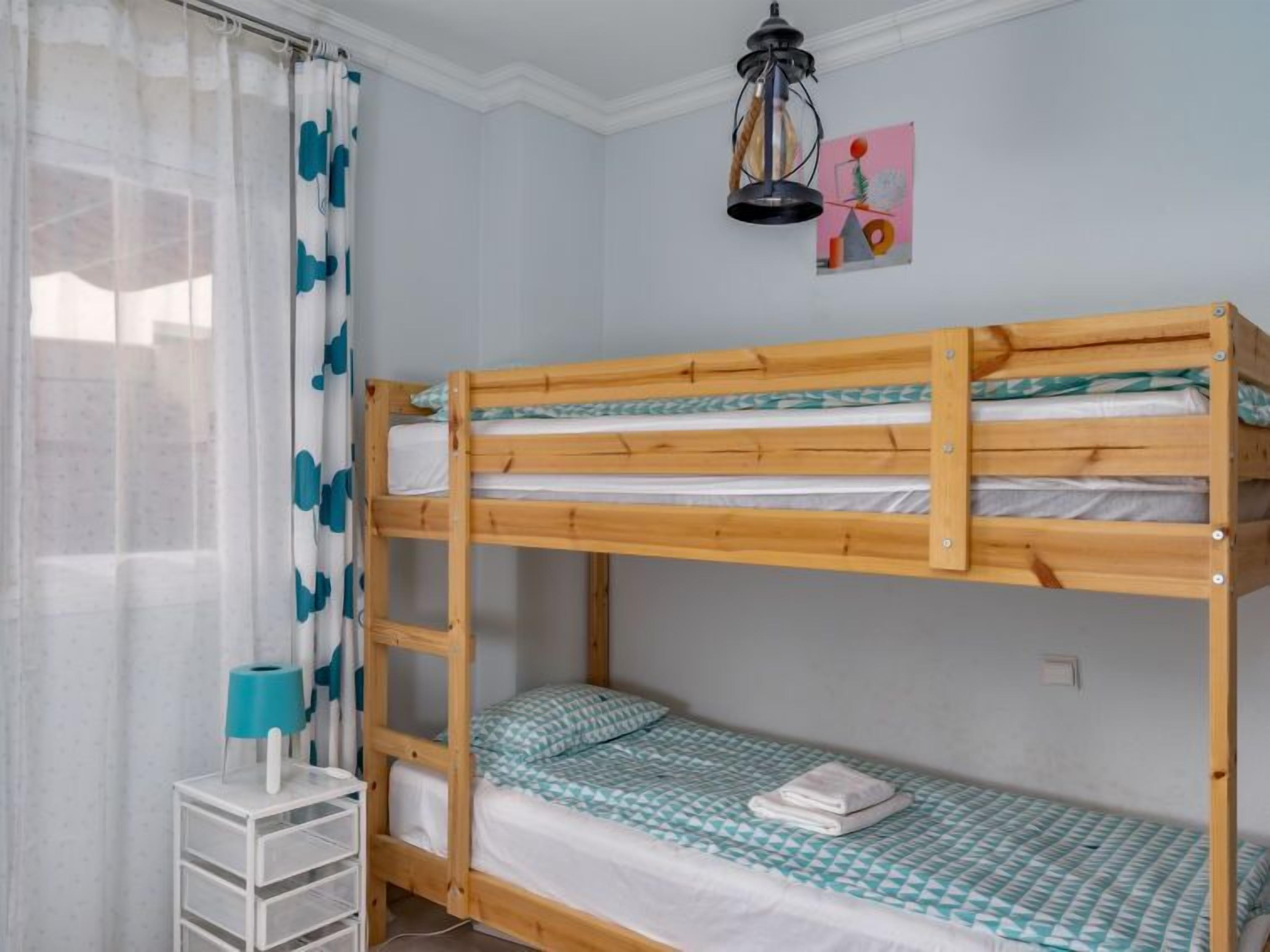 Une chambre avec un lit superposé, un bureau blanc et une lampe.