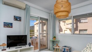 Un salon moderne avec un téléviseur à écran plat posé sur un meuble TV blanc, un canapé beige, une petite table ronde et un luminaire suspendu en osier.