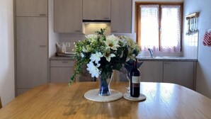 A kitchen with wooden cabinets, a dining table with a vase of flowers and a bottle of wine.