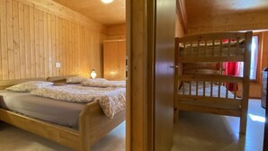 A wooden cabin room with a bed, a nightstand, and a window with red curtains.