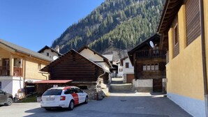 A street with traditional wooden houses, a parked car, and a mountain in the background. - Della Posta Stambecco by Interhome (Rossa)