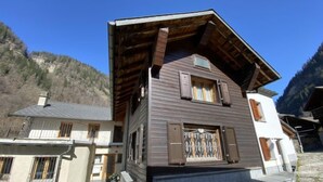 A two-story wooden house with a stone foundation, a balcony, and a window with shutters. - Della Posta Stambecco by Interhome (Rossa)